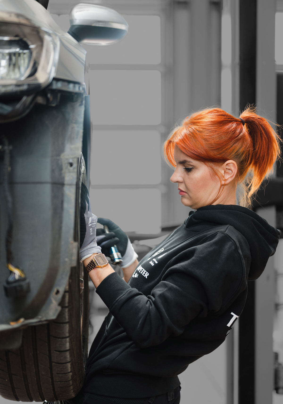 Die Kfz-Mechatronikerin Anne Althaus-Braun wechselt eine Reifen an einem aufgebocktem Auto (Ansicht von der Seite).