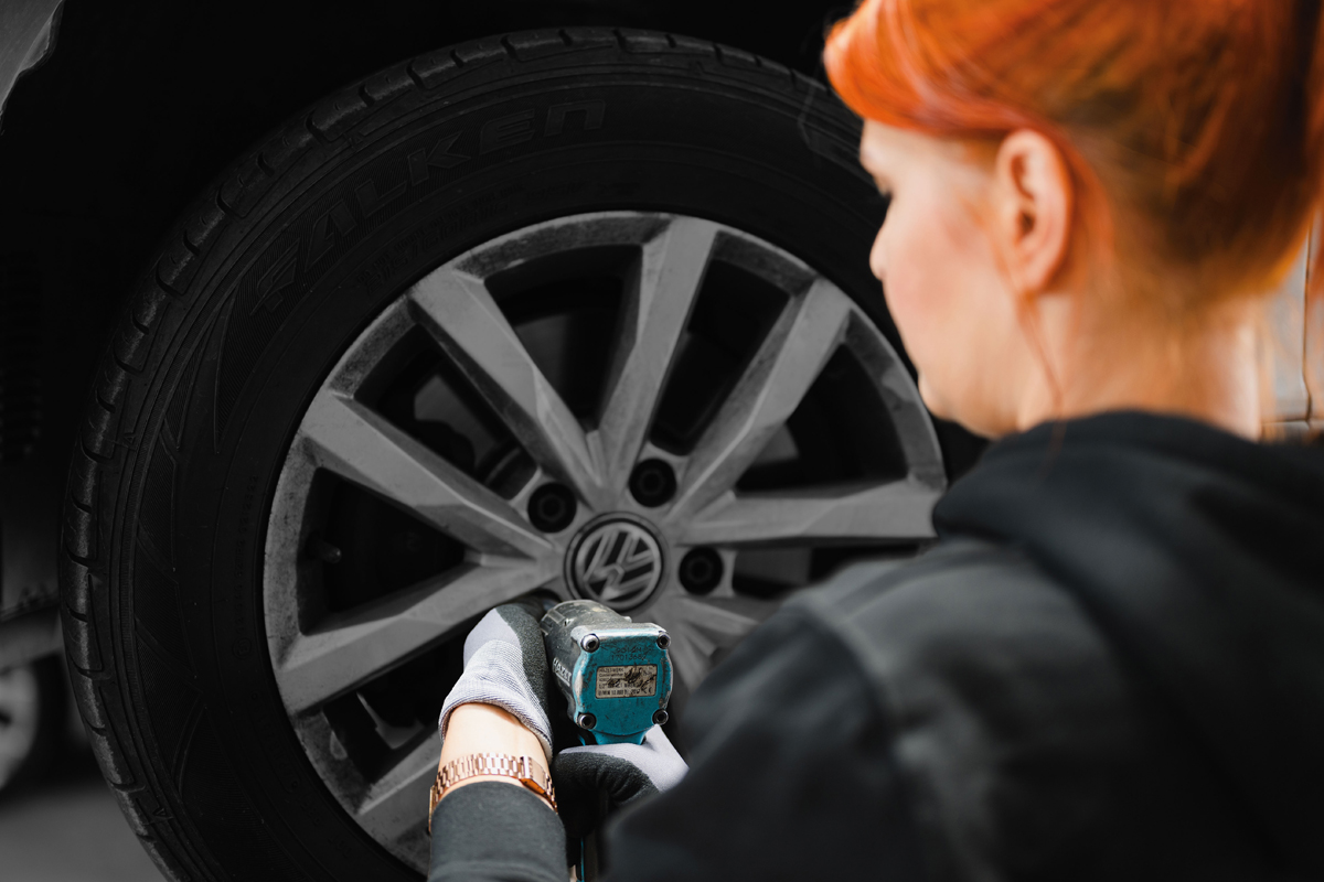 Die Kfz-Mechatronikerin Anne Althaus-Braun wechselt eine Reifen an einem aufgebocktem Auto (Ansicht über ihre Schulter).