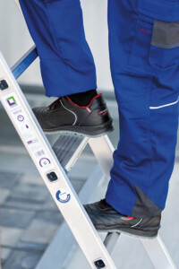 Eine Person in blauer Arbeitshose und schwarzen Arbeitsschuhen steht auf einer Leiter.