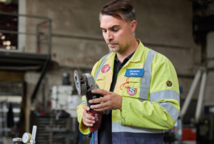 Ein Mann in gelber Arbeitsjacke inspiziert ein Schleifgerät.