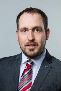 Ein Mann mit Anzug guckt in die Kamera.
