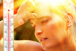 Eine verschwitzte Frau wischt sich unter grellem Sonnenlicht die Stirn, während ein Thermometer am Bildrand Temperaturen über vierzig Grad Celsius anzeigt.