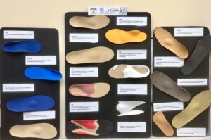 Wandtafel mit vielen farbigen orthopädischen Einlegesohlen, jede mit kleinem Etikett zu Material und Einsatzbereich.