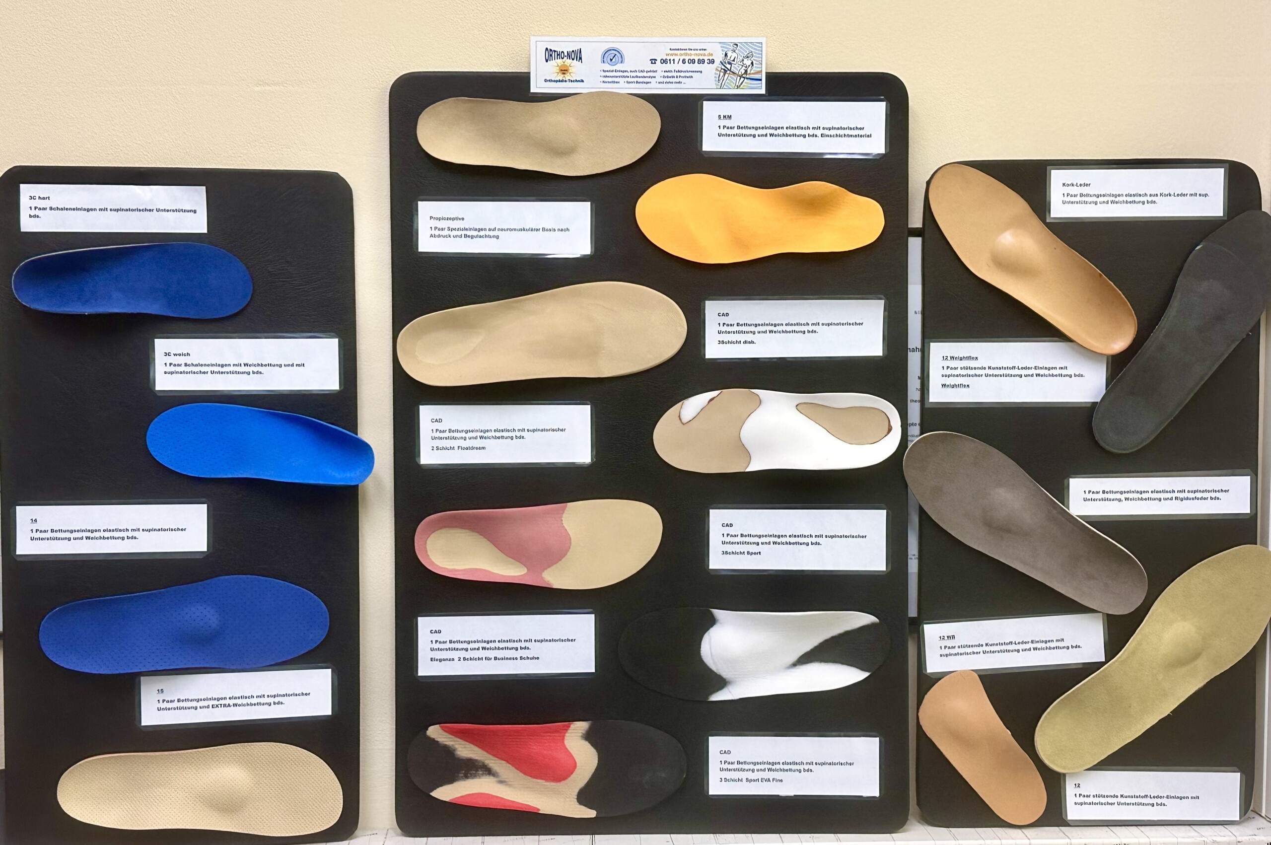 Wandtafel mit vielen farbigen orthopädischen Einlegesohlen, jede mit kleinem Etikett zu Material und Einsatzbereich.