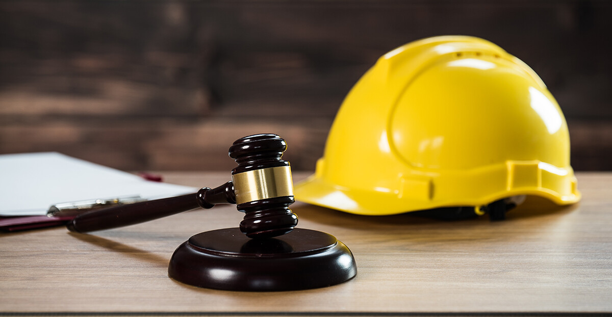 Ein Richterhammer liegt auf einem Schreibtisch neben einem gelben Schutzhelm.