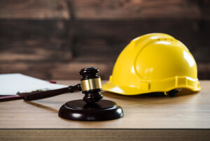 Ein Richterhammer liegt auf einem Schreibtisch neben einem gelben Schutzhelm.