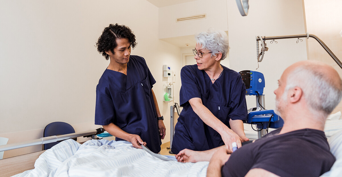 Zwei Pflegende untersuchen am Patientenbett den Blutdruck eines Patienten.