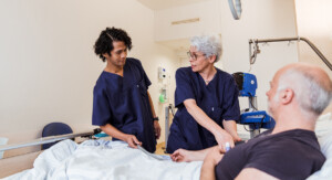 Zwei Pflegende untersuchen am Patientenbett den Blutdruck eines Patienten.