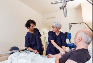 Zwei Pflegende untersuchen am Patientenbett den Blutdruck eines Patienten.