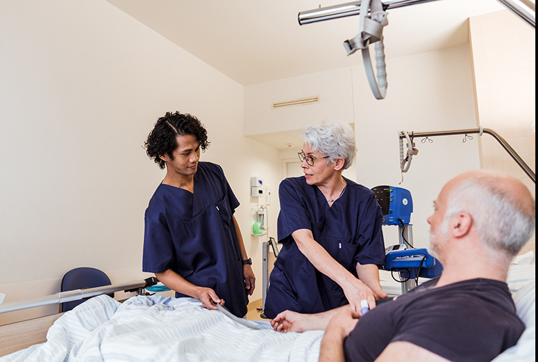 Zwei Pflegende untersuchen am Patientenbett den Blutdruck eines Patienten.