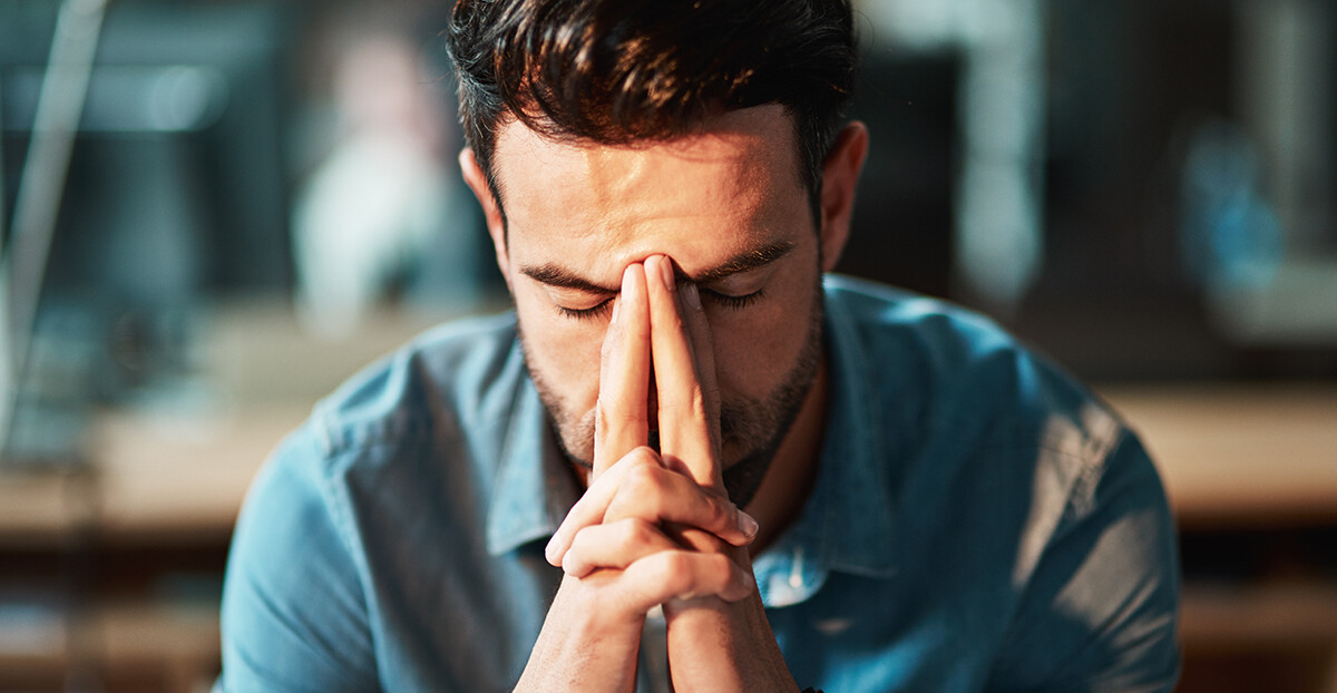 Mann presst die Hände nachdenklich ans Gesicht und wirkt erschöpft oder gestresst.