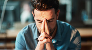 Mann presst die Hände nachdenklich ans Gesicht und wirkt erschöpft oder gestresst.