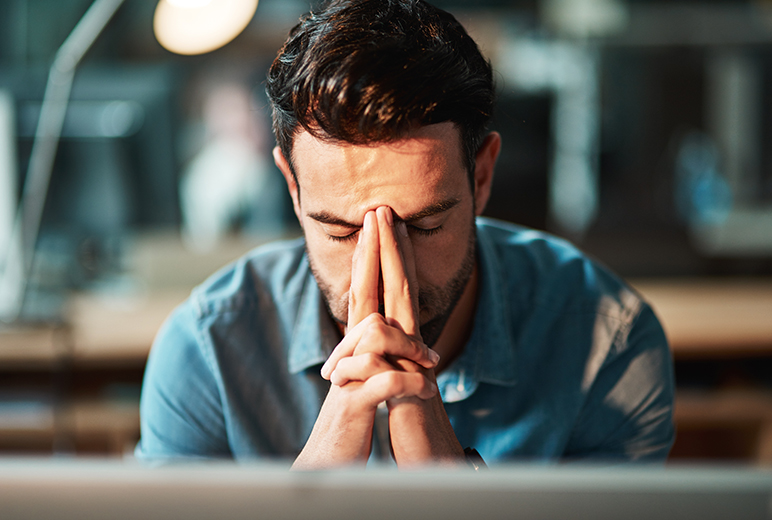 Mann presst die Hände nachdenklich ans Gesicht und wirkt erschöpft oder gestresst.