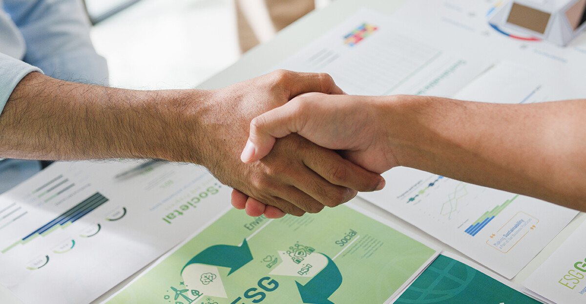 Händedruck über Unterlagen mit ESG-Grafiken.