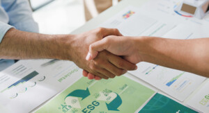 Händedruck über Unterlagen mit ESG-Grafiken.