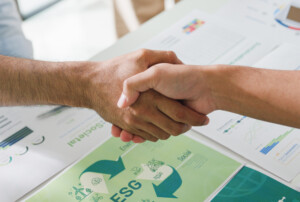 Händedruck über Unterlagen mit ESG-Grafiken.