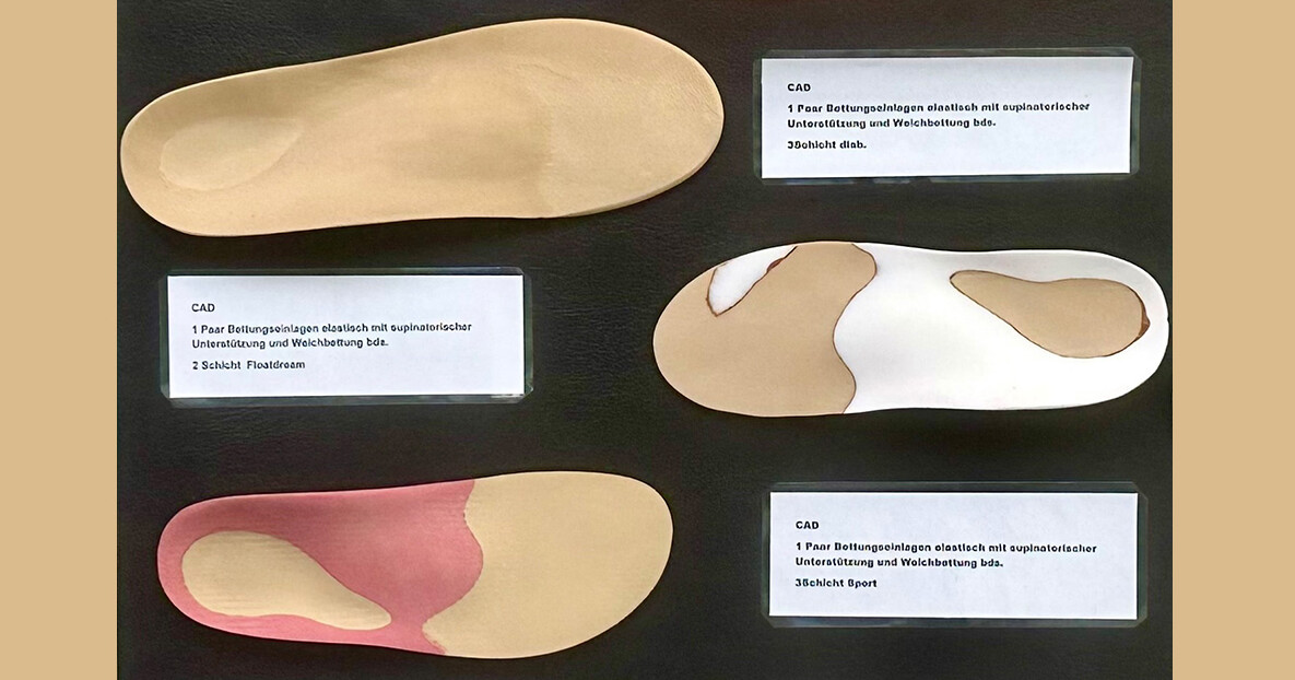Nahaufnahme einer Präsentationswand mit mehreren orthopädischen Einlagen in unterschiedlichen Formen und Farben; kleine Beschriftungsschilder erklären die Modelle.