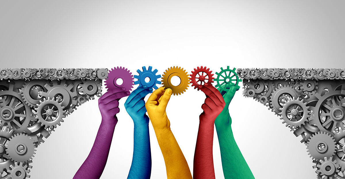 Mehrere farbige Hände halten Zahnräder, die zwei Zahnradflächen zu einer Brücke verbinden.