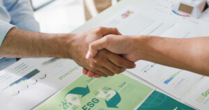 Händedruck über Unterlagen mit ESG-Grafiken.