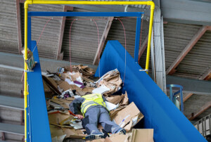 Papierpresse, in der ein Mann mit Warnweste liegt.